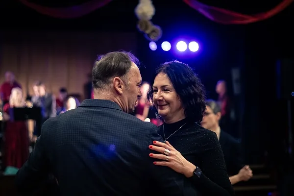 Tančící pár středního věku, žena s rudými nehty se usmívá, v pozadí modré reflektory a účinkující.